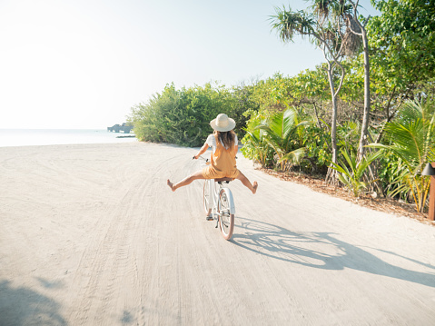 Tropical vacations young woman with bicycle in the Maldives. Female enjoying bike ride on sandy island. Dreamlike destination