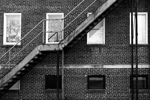 a back alley rusted fire escape stairs black and white windows brick building