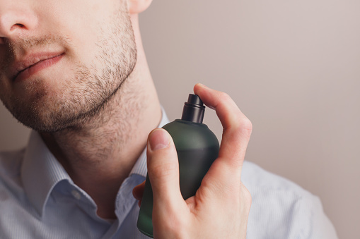 Handsome unshaven man applying perfume on neck, closeup. Pheromones and fragrance