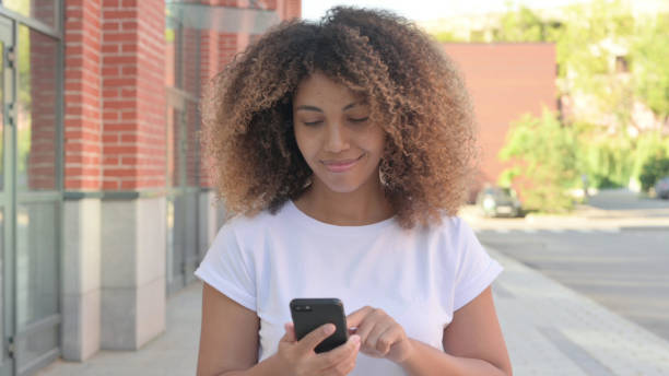 istock Young African Woman Browsing Internet on Smartphone while Walking Outside 1364626034