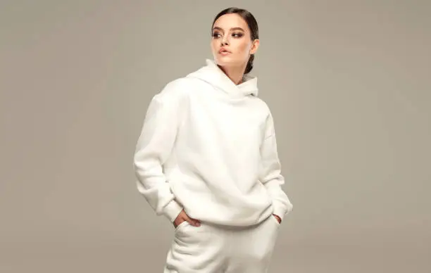 Photo of White hoody and sport pants on the perfectly looking young woman wearing in splendid makeup. Fashion and sport.
