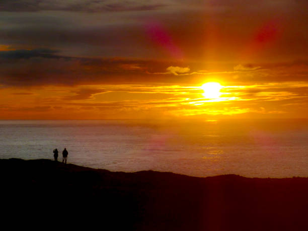 istock Two people in silhouette on clifftop watching sunset over sea 1364631876
