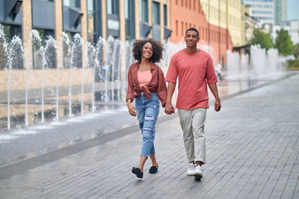 Dark-skinned man and woman holding hand walking stock photo