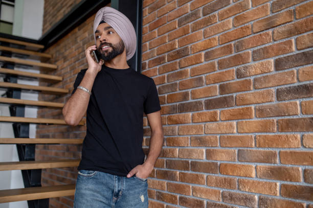 Indian man in beige turban standing on stairs and talking on the phone stock photo