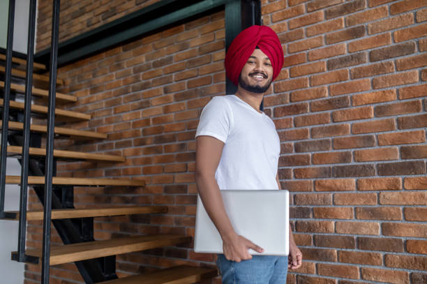 Young indian man in red turban standing on stairs Work from home. Young indian man in red turban standing on stairs turban stock pictures, royalty-free photos & images