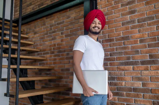 Work from home. Young indian man in red turban standing on stairs