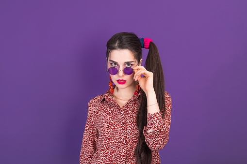 Portrait of cute young brunette dressed in 90s style on purple studio background.