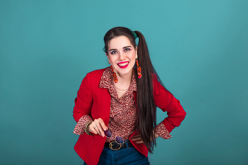 Smiling young brunette woman in 90s style in red jacket on blue background.