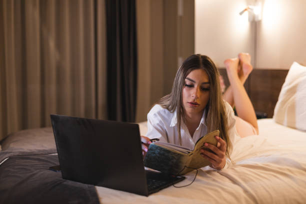 istock Young businesswoman lying down in a hotel room while working on her laptop and taking notes in her notepad 1364641158