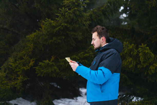 jeune randonneur en veste bleue perdu dans une montagne brumeuse et enneigée en regardant la carte - trail marker hiking sign sports and fitness photos et images de collection