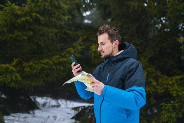 jeune randonneur en veste bleue perdu dans une montagne brumeuse et enneigée en regardant la carte et son smartphone - trail marker hiking sign sports and fitness photos et images de collection