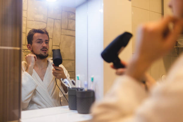jeune homme en peignoir se séchant les cheveux après une douche dans un miroir de salle de bain brumeux - toothbrush brushing teeth brushing dental hygiene photos et images de collection