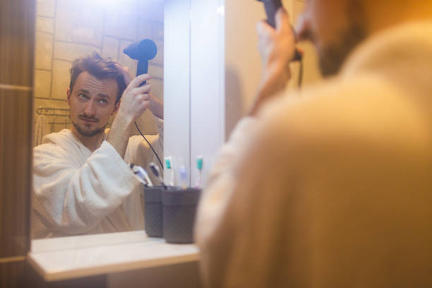 jeune homme en peignoir se séchant les cheveux après une douche dans un miroir de salle de bain brumeux - toothbrush brushing teeth brushing dental hygiene photos et images de collection