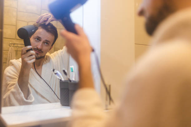 jeune homme en peignoir se séchant les cheveux après une douche dans un miroir de salle de bain brumeux - brushing teeth photos et images de collection