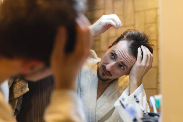 istock Young man in a bathrobe checking his balding patterns in the bathroom mirror after a shower 1364642568
