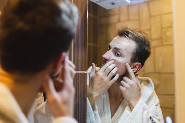 jeune homme en peignoir faisant éclater des boutons tout en se regardant dans le miroir après une douche - toothbrush brushing teeth brushing dental hygiene photos et images de collection