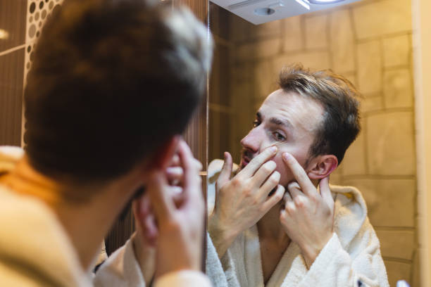 jeune homme en peignoir faisant éclater des boutons tout en se regardant dans le miroir après une douche - toothbrush brushing teeth brushing dental hygiene photos et images de collection