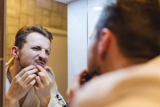 jeune homme en peignoir faisant éclater des boutons tout en se regardant dans le miroir après une douche - brushing teeth photos et images de collection