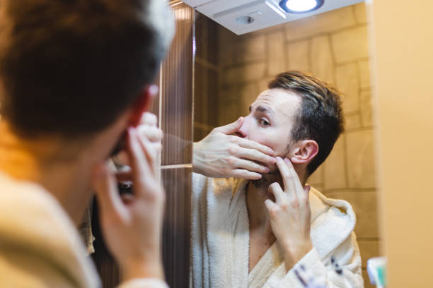 jeune homme en peignoir faisant éclater des boutons tout en se regardant dans le miroir après une douche - toothbrush brushing teeth brushing dental hygiene photos et images de collection