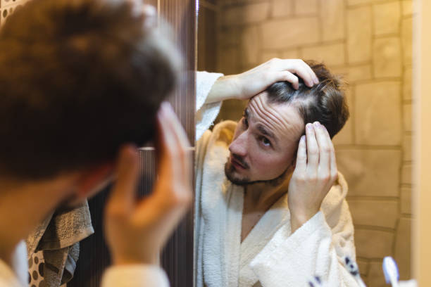 jeune homme en peignoir vérifiant ses motifs chauves dans le miroir de la salle de bain après une douche - toothbrush brushing teeth brushing dental hygiene photos et images de collection