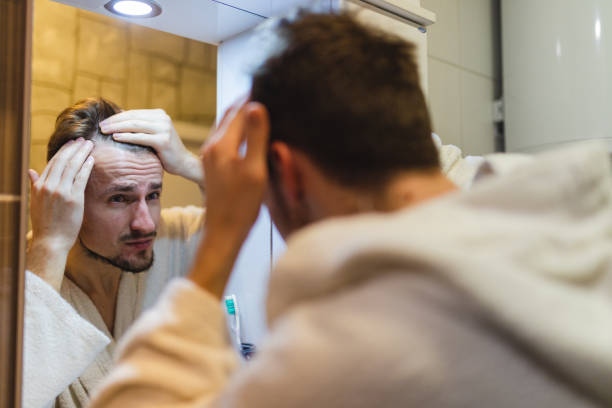 istock Young man in a bathrobe checking his balding patterns in the bathroom mirror after a shower 1364642608