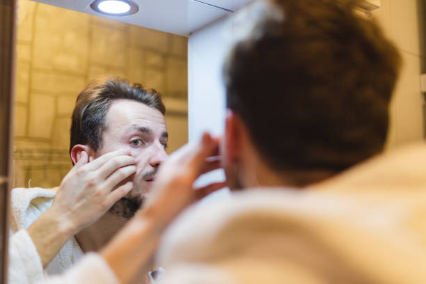 jeune homme en peignoir faisant éclater des boutons tout en se regardant dans le miroir après une douche - toothbrush brushing teeth brushing dental hygiene photos et images de collection