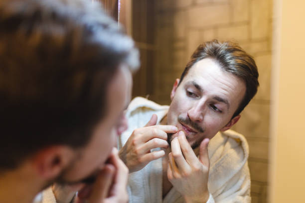 istock Young man in a bathrobe popping pimples while looking at himself in the mirror after a shower 1364643253