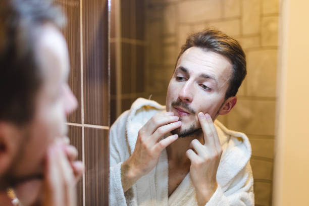 jeune homme en peignoir faisant éclater des boutons tout en se regardant dans le miroir après une douche - brushing teeth photos et images de collection