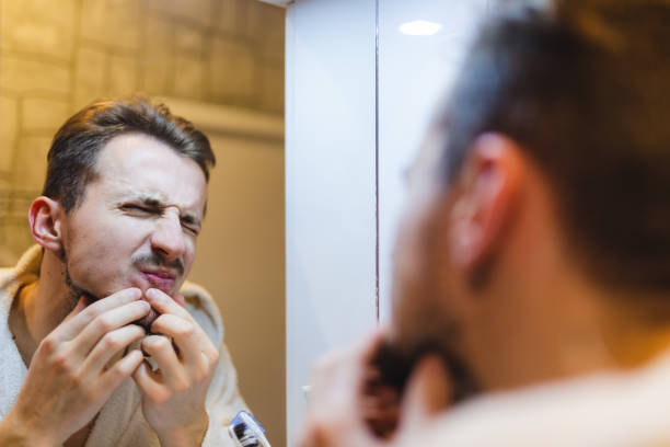 istock Young man in a bathrobe popping pimples while looking at himself in the mirror after a shower 1364643260