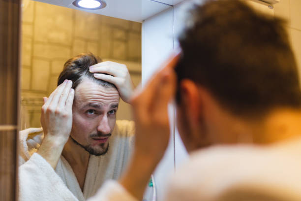 istock Young man in a bathrobe checking his balding patterns in the bathroom mirror after a shower 1364643278