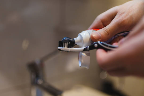 gros plan d’une personne mettant du dentifrice sur une brosse à dents au-dessus de l’évier de la salle de bain - brushing teeth photos et images de collection