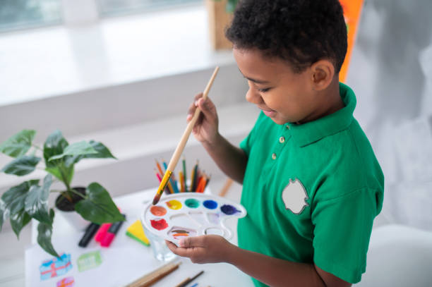 istock Smiling boy looking at palette and brush in hand 1364643431