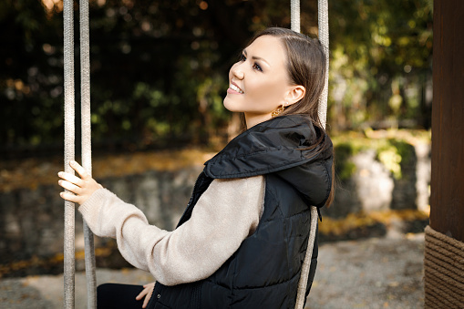 Young dreamy woman sitting on swing in autumn in park outdoors. High quality photo