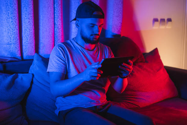 istock Young bearded man using his tablet for gaming with RGB lights in the background while relaxing at home 1364643718