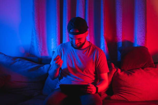 istock Young bearded happy man using his tablet for gaming with RGB lights in the background while relaxing at home 1364643719