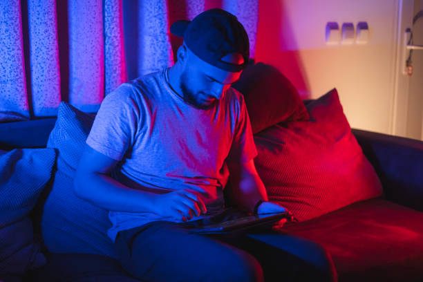 istock Young bearded man using his tablet for gaming with RGB lights in the background while relaxing at home 1364643826