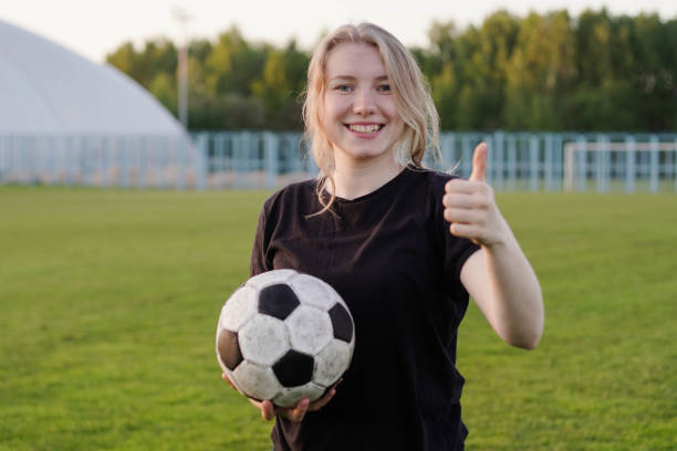 молодая девочка-футболист, держащая футбольный мяч большим пальцем вверх - youth league стоковые фото и изображения
