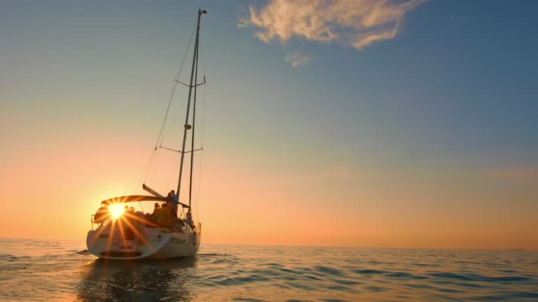 Slow motion wide shot of a sailing yacht gliding gently across the sea at sunset. Shot in Slovenia.