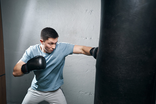 Caucasian boxer with pain and injury after intense boxing training or fighting match, sitting at the edge of ring. Physical injury in sport concept. Impetus