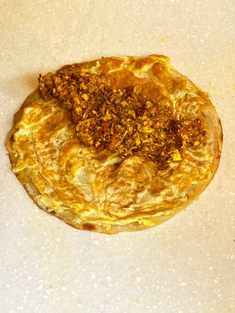 istock Close-up image of a paratha (flatbread) topped with paneer ready to be folded into a Frankie (Mumbai Burrito), elevated view, focus on foreground 1364650187