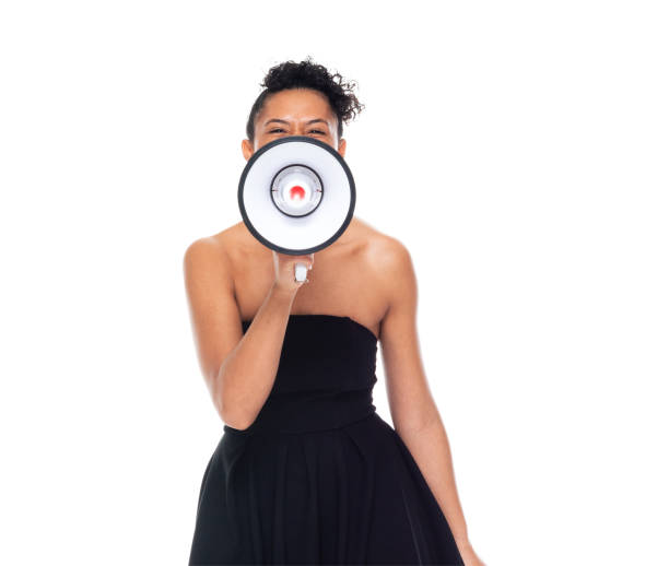 African-american ethnicity young women standing in front of white background wearing dress and holding megaphone stock photo