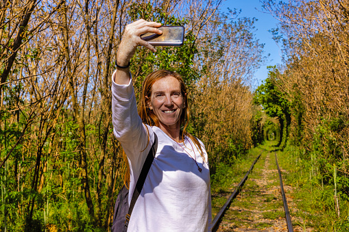 Tourist woman takes a selfie on the railway tracks with vegetation tunnel in the background
