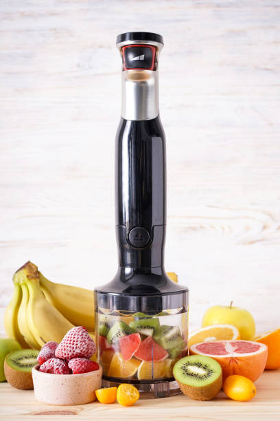 istock Black plastic electrical hand blender and accessories with sliced fruit on a wooden background, verticall. 1364669595
