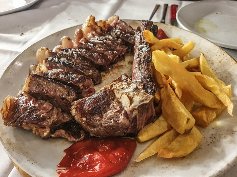 Close-up view of T-bone steak with potatoes and roasted red peppers. Roasted high quality T-Bone steak on white tablecloth table.