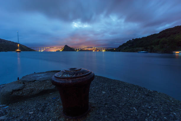 bollard no píer à noite com ponte ao fundo levando à ilha krk, croácia - sailboat pier bridge storm - fotografias e filmes do acervo