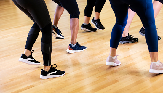 Cropped view of the legs of five multi-ethnic women taking a dance exercise class. They are wearing black leggings or yoga pants and athletic shoes. They are dancing, stepping in unison.