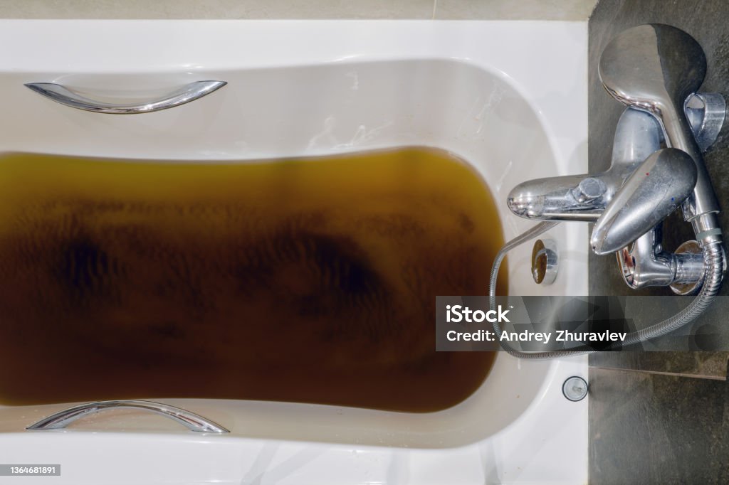 A bathtub filled with dirty water due to a clogged sewer pipe, close-up Clogged Stock Photo