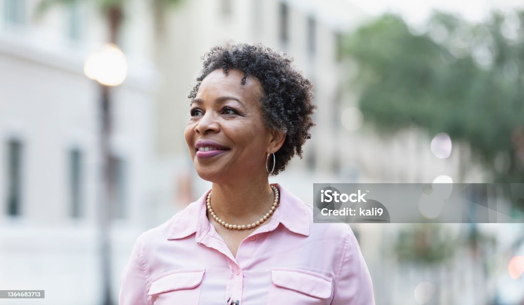 Headshot of mature black woman walking on city street Headshot of a mature black woman walking outdoors in the city, smiling confidently, looking away from the camera. One Woman Only Stock Photo