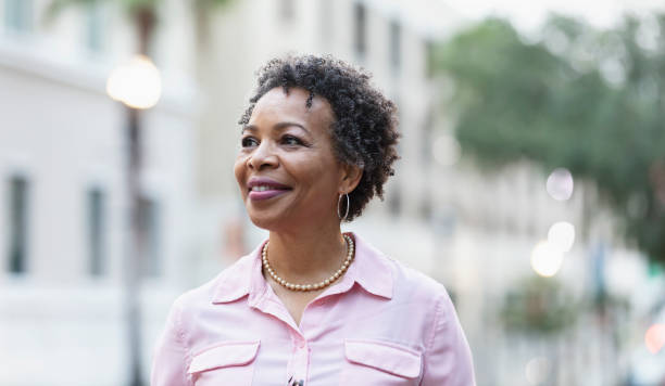 Headshot of mature black woman walking on city street Headshot of a mature black woman walking outdoors in the city, smiling confidently, looking away from the camera. candid stock pictures, royalty-free photos & images