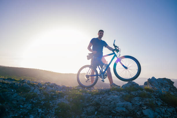 istock Mountain biker holding his bike on a rough cliff terrain on a sunset. 1364685268